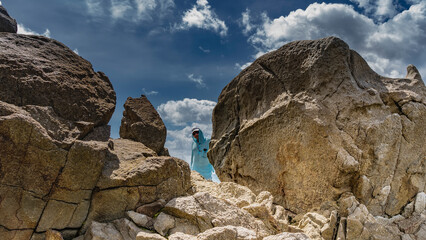 Huge weathered granite boulders against a background of blue sky and clouds. In the gap between the stones there is a man in a cap, sunglasses and smiling. Seychelles