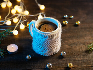 A cup of coffee in a knitted jacket on a wooden table. Winter home atmosphere