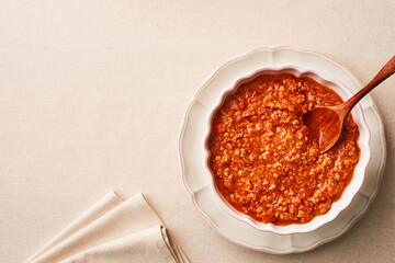A bowl of fresh BOLOGNESE SAUCE on a linen tablecloth with copy space. Studio shot. Top view.