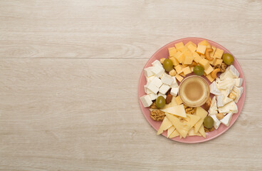 Cheese plate with olives aand nuts on wooden background, top view