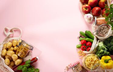 Eco bags with assorted fruits and vegetables and groceries jars on pink surface
