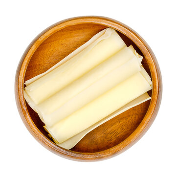 Swiss hard cheese rolls, in a wooden bowl. Three rolled thin slices of Sbrinz, extra hard full fat cheese, produced in central Switzerland, often used instead of Parmesan cheese. Close up, from above.