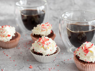 Coffee with muffins, muffins with cream and sprinkles. On a concrete background