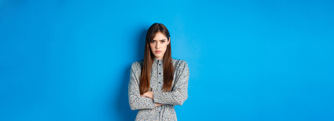 Angry frowning woman in dress, cross arms on chest and feel offended about something unfair,...