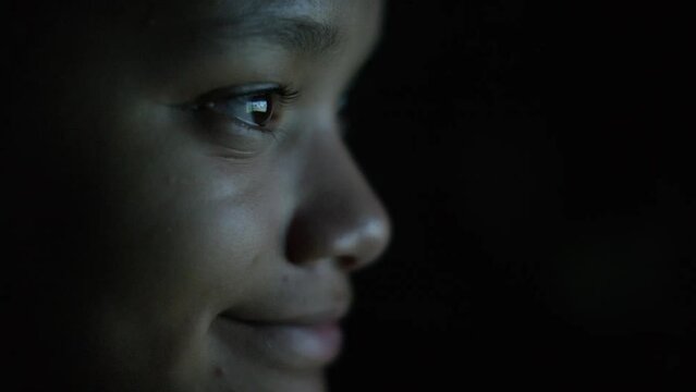 Close handheld shot of young female teenager watching something on a screen in the dark