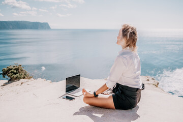 Fototapeta premium Woman sea laptop yoga. Business woman freelancer in yoga pose working over blue sea beach at laptop and meditates. Girl relieves stress from work. Freelance, digital nomad, travel and holidays concept
