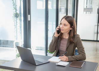 Obraz premium Marketing, Finance, Accounting, Planning, Businesswoman of bi nationality is talking with a customer representing a company distributor using a smartphone with laptop pen and notepad on office desk.