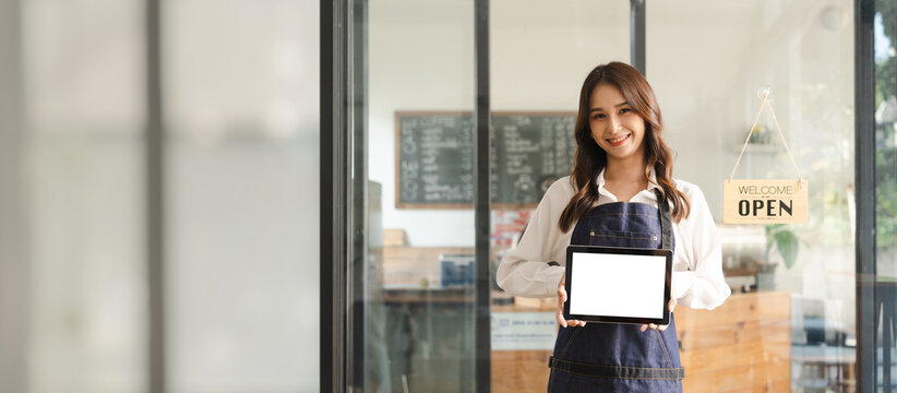 Young asia business owner woman with apron with open sign at café, open again, blank white screen tablet pc computer, looking to camera.