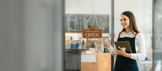 Young friendly female pretty caucasian coffee shop woman owner in apron with open sign, small business owners smiling and service take away orders from food delivery application on tablet.