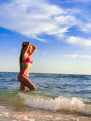 A young beautiful woman with long hair in a swimsuit dreamily looks at the beach with the sea in the background