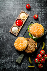 Burgers with French fries, gherkins,tomatoes and different sauces.