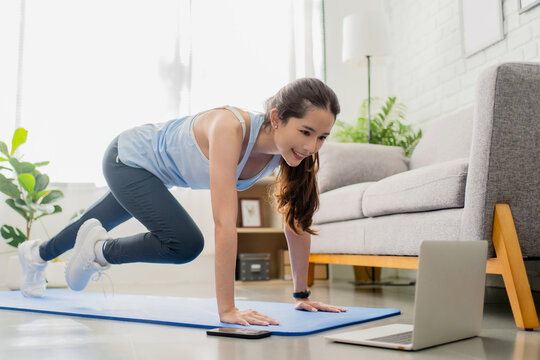 Asian young healthy woman workout yoga online class by laptop in morning. Fitness exercise concept at home.