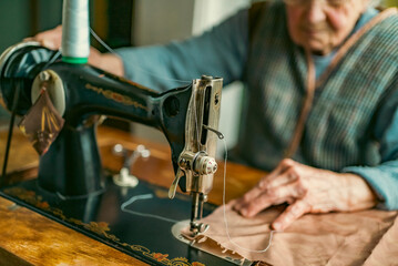Senior woman in spectacles use sewing machine. wrinkled hands of the old seamstress.elderly woman . Old sewing machine Classic retro style manual sewing machine ready for sewing work.
