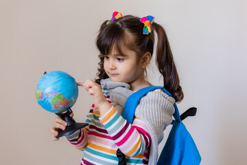 a happy little preschool girl with a backpack and a globe on a light background, space for text. Preschool education, traveling with children