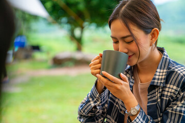 Young Asian woman relax and enjoy outdoor lifestyle camping in forest mountain on summer holiday travel vacation. Attractive girl drinking coffee while having breakfast at the camp in the morning.
