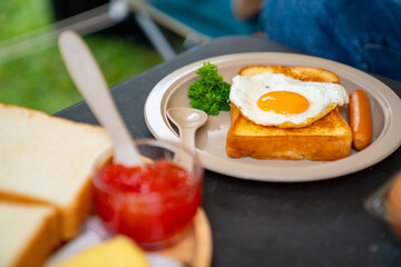 Breakfast on the table. Asian couple cooking food fried egg and bread with sausage at camp. Man and woman enjoy outdoor lifestyle travel nature and camping together on summer holiday vacation.