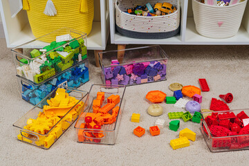 Colorful rainbow colored constructor pieces in transparent plastic boxes in childrens room. Bright stackable plastic toy bricks sorting by colors. Space organizing at childrens room.