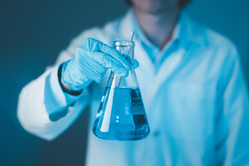 Scientist hand hold erlenmeyer flask with stirring rod filled with blue sample chemicals in...