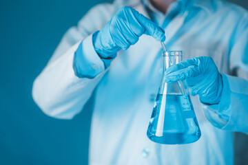Scientist hand hold erlenmeyer flask with stirring rod filled with blue sample chemicals in...