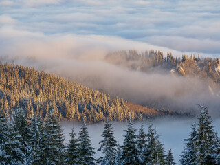 Aerial view of distant mountain peaks above clouds in clear sunny blue sky.