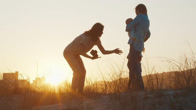 Family photographer. Woman with camera takes picture of the mother with kids at sunset. Family with kids on outdoor photoset on the urban background