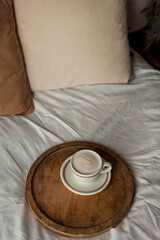 Hot mug of cappuccino on wooden tray on the bed, breakfast. Cozy house. Beige natural colors....