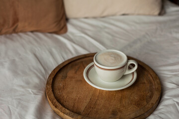 Hot mug of cappuccino on wooden tray on the bed, breakfast. Cozy house. Beige natural colors....