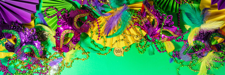 Mardi Gras colourful holiday greeting card background with festival masquerade accessories, decor, carnival mask, beads, feathers, fan on bright background traditional yellow purple green colors