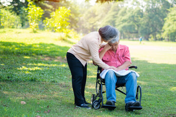 Fototapeta premium Senior couple in the park and wife taking care of a husband in a wheelchair a patient with paralysis, with his wife comforting and encouraging each other. Retirement health insurance concept.
