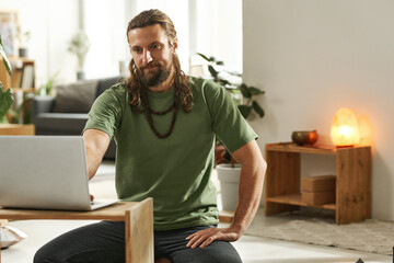 Young man watching yoga lesson online using his laptop computer while sitting in the room at home