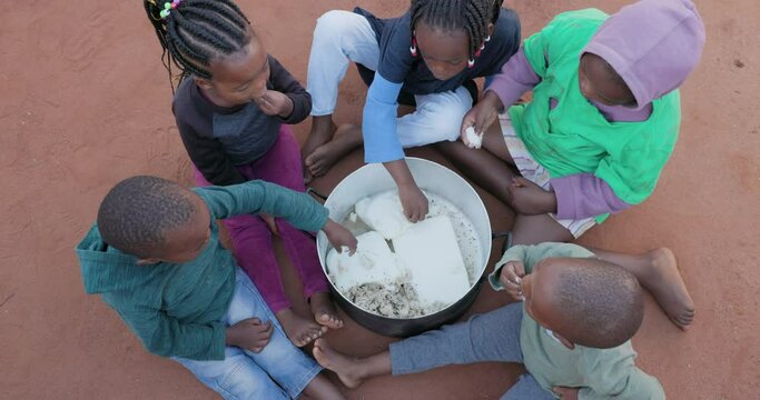 Poverty in Africa. Small group of starving Black African children eating maize from a communal cooking pot