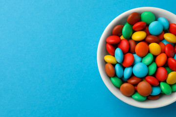 Bowl with tasty colorful candies on blue background, top view. Space for text