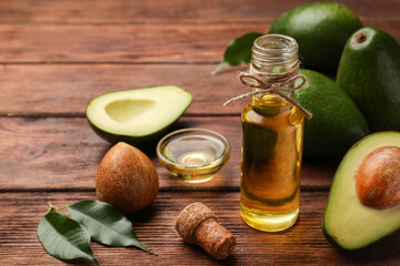 Glass bottle of cooking oil and fresh avocados on wooden table, closeup