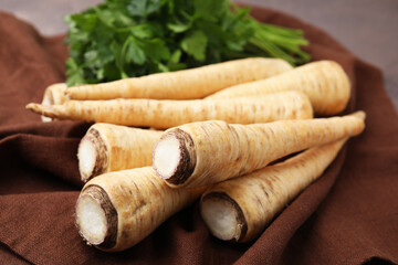 Whole raw parsley roots and fresh herb on brown fabric, closeup