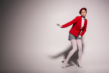 Full length of trendy asian model in gloves and jacket posing on grey background