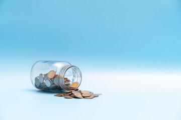 A lot of money coin flow out of the glass jar on blue background, Saving money concept.