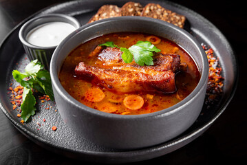 Solyanka soup with meat, sausage, vegetables, olives and lemon in bowl on wooden table background