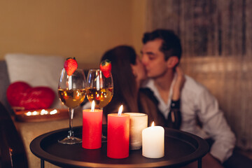 Valentines Day couple kissing at home. Close up of festive drinks wine with strawberries by burning red candles.