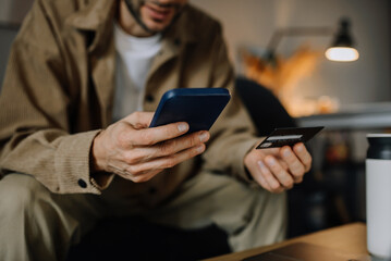 Man holding credit card and using smartphone at home 