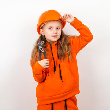 A Little Girl In An Orange Suit And A Construction Helmet, Holding An Adjustable Wrench, A Concept Of Young Worker. Portrait, White Background, Labor Day.