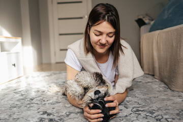 Portrait of a young caucasian woman with vitiligo playing with her little black dog miniature schnauzer breed on the floor at home. Cute puppy hugs with his owner. Friendship concept 
