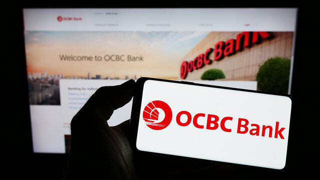 Stuttgart, Germany - 01-12-2023: Person holding smartphone with logo of Oversea-Chinese Banking Corporation (OCBC Bank) on screen in front of website. Focus on phone display.