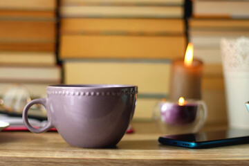Notebook, pen, tablet, reading glasses, books, phone, candle, bowl of biscuits and cup of tea on the table. Selective focus.