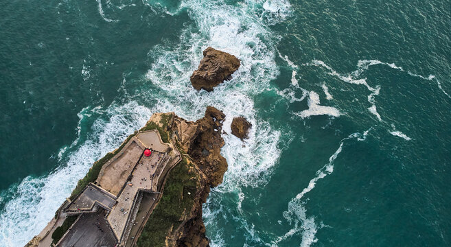Aerial view of an old lighthouse on a cliff with a fortress on the coast of the Atlantic ocean in Nazare town, Portugal. High quality photo