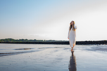 beautiful young Women is walking a beach with sunlight and water in background ans looking over the sea with hand in her hair