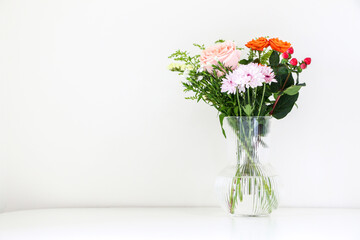 Beautiful bouquet of flowers with pink and orange roses and white chrysanthemum, on right of white table against white background, with copy space