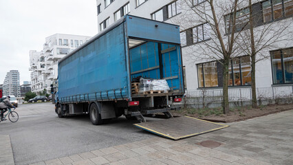 Large delivery truck with tailgate open with goods in the cargo hold in front of an office building.