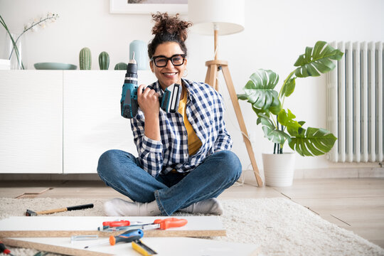 Black woman holding electric drill tool to assembly furniture in new home