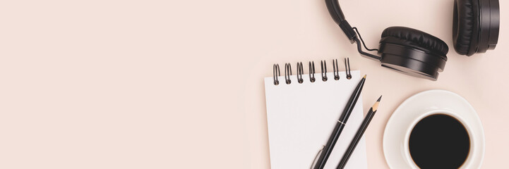 Banner with cup of coffee, headphones, notepad and stationery on a beige background.