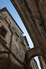Narrow street between two medieval stone buildings joined by a stone and brick arch, in Italy - 562450155
